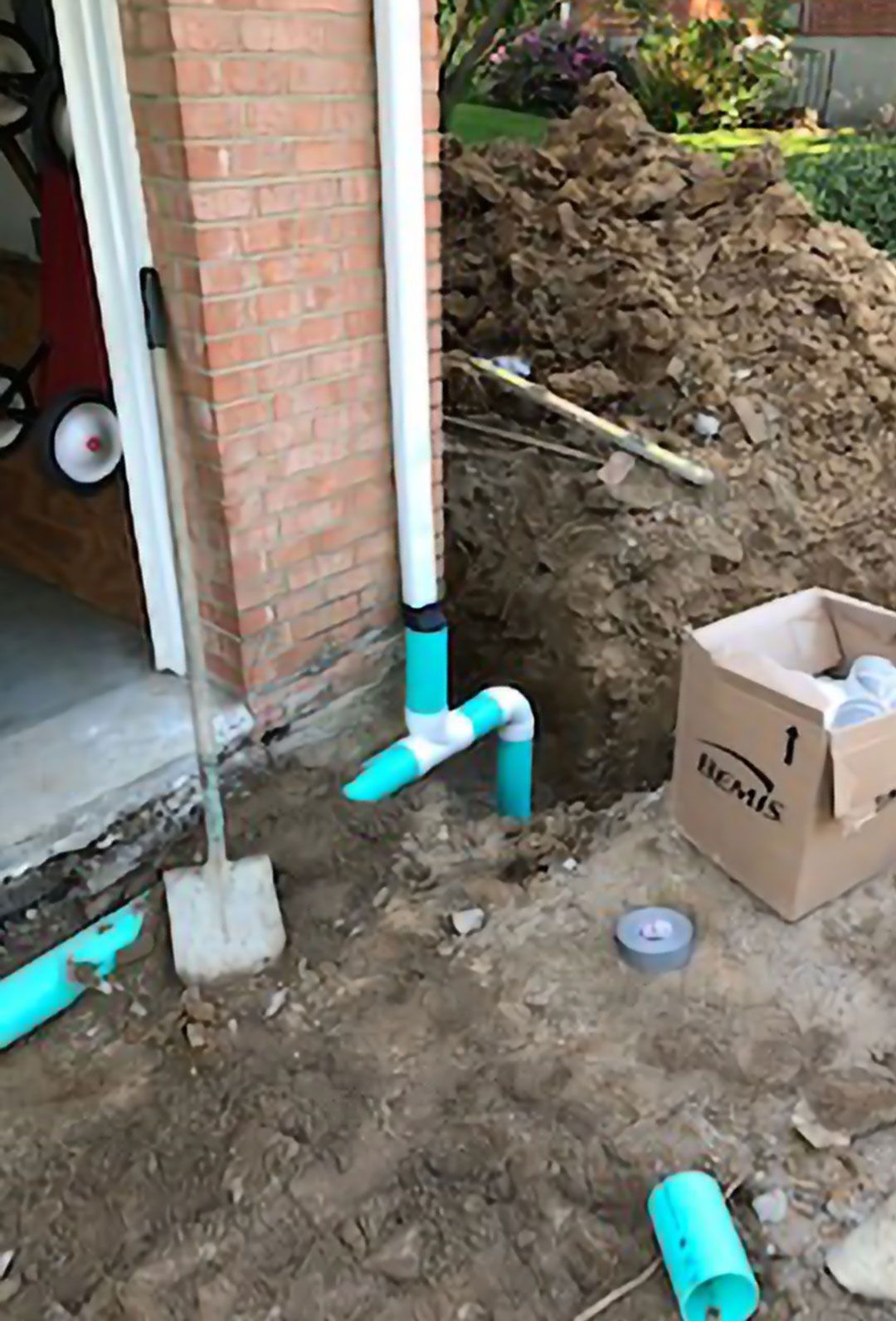 A box is sitting in the dirt next to a drain pipe.