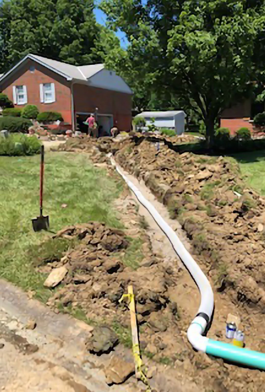 A large pipe is being installed in the dirt in front of a house.