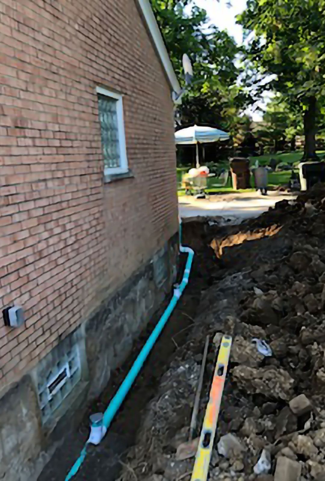 A drain pipe is being installed on the side of a brick house.