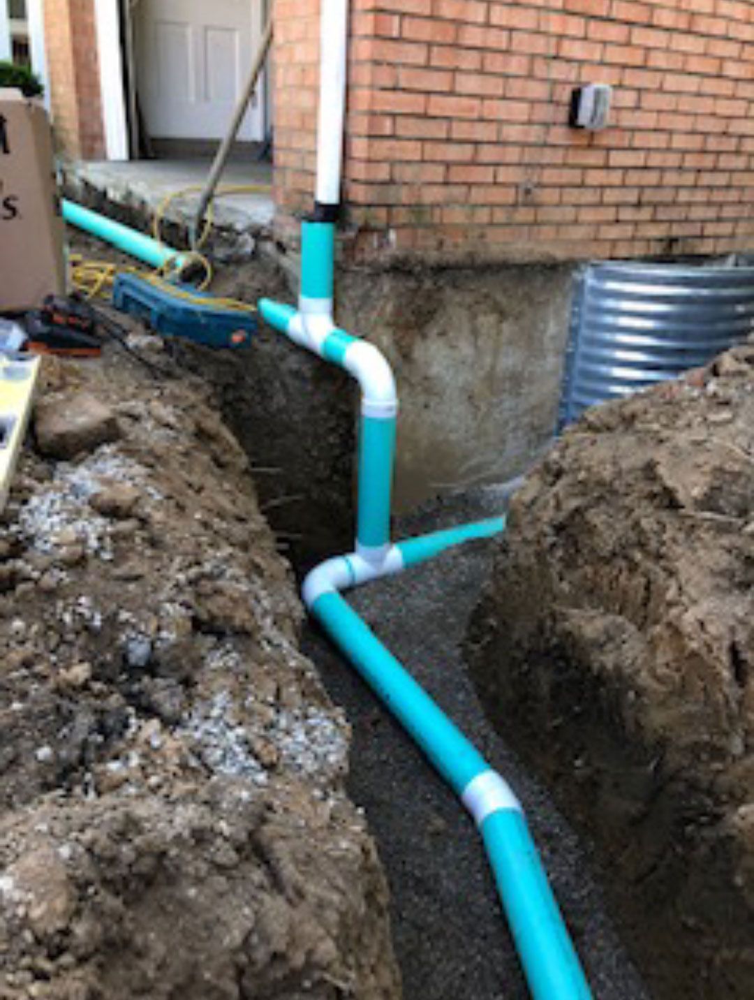 A drain pipe is being installed in a trench next to a brick building.