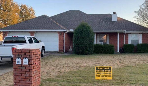 Red brick house with white garage doors; white truck in driveway; yard sign in grass.