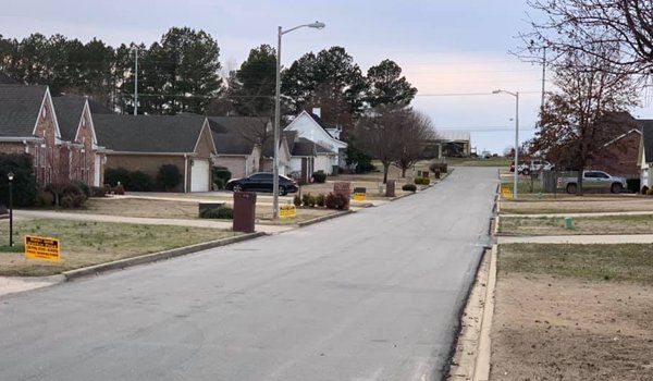 Suburban street lined with houses and bare trees under a cloudy sky.