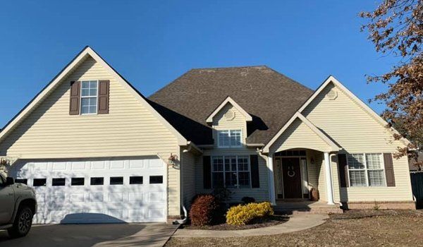 Beige house with white garage door and brown roof on a sunny day.