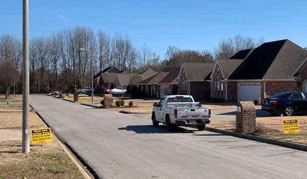 A white pickup truck parked on a residential street with houses and a bright blue sky.