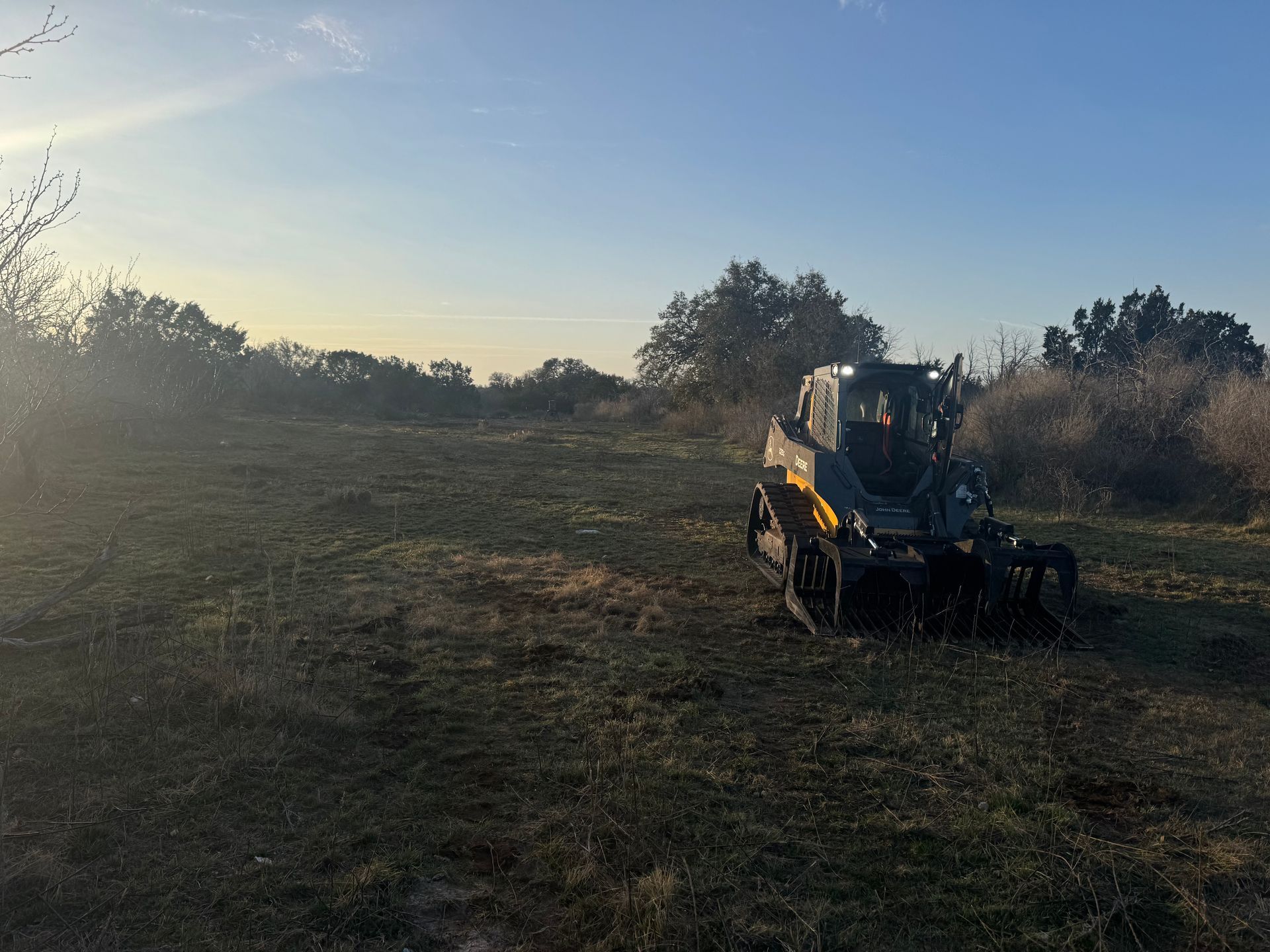 Yellow and black tracked vehicle on a grassy field, trees in the background under a blue sky.