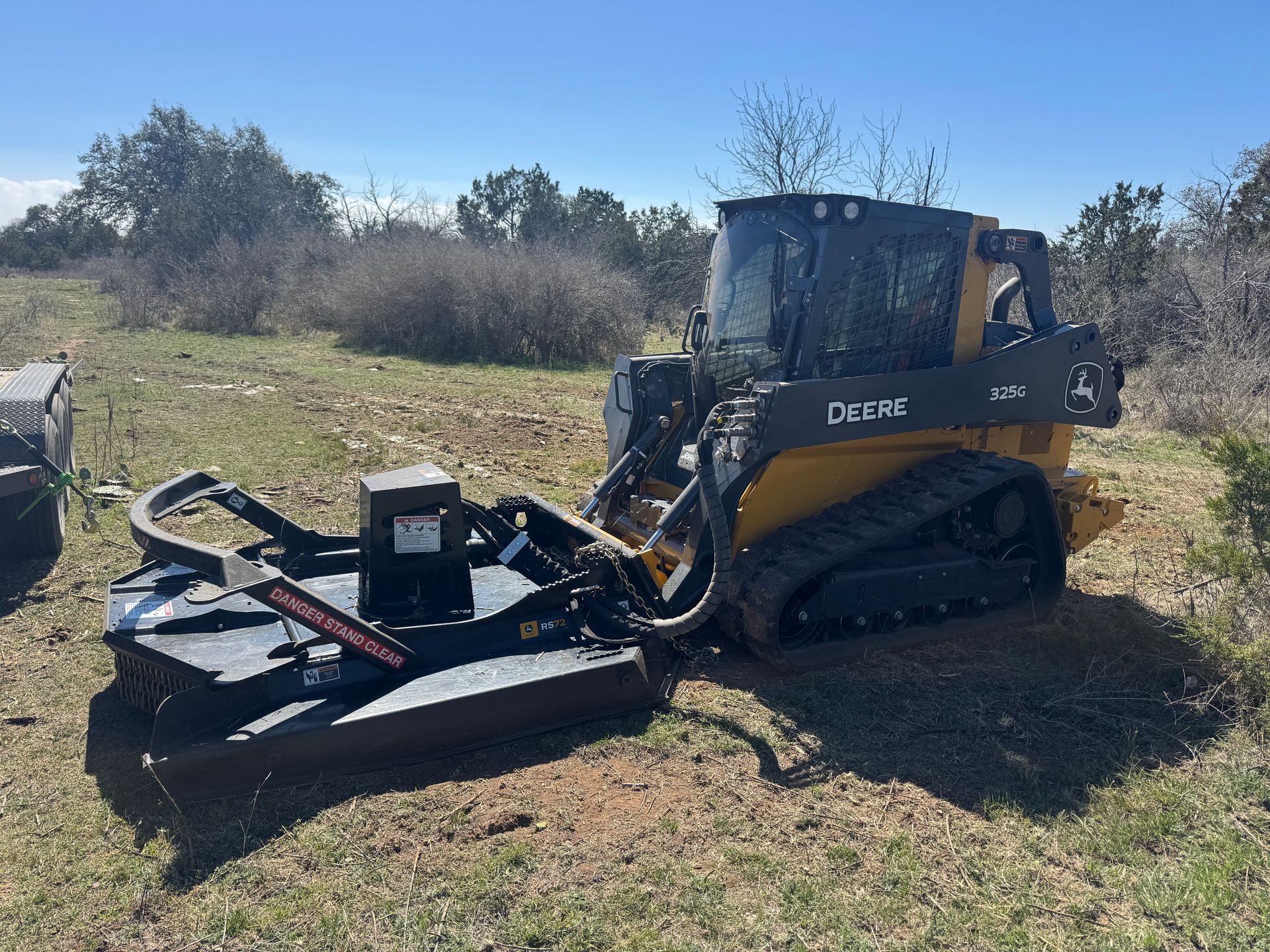 Yellow and black John Deere skid steer with brush cutter in a field.