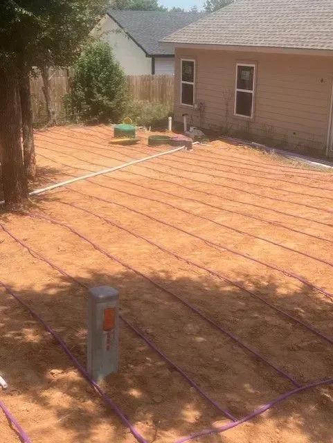 Purple irrigation lines laid out in a sandy yard behind a beige house.