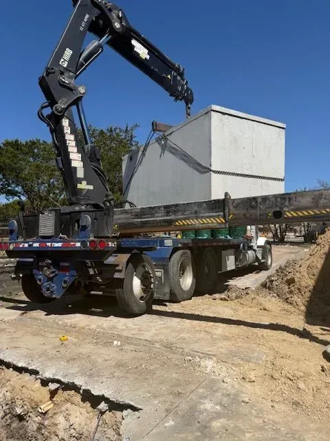 A crane lifting a large concrete box off a flatbed truck at a construction site.
