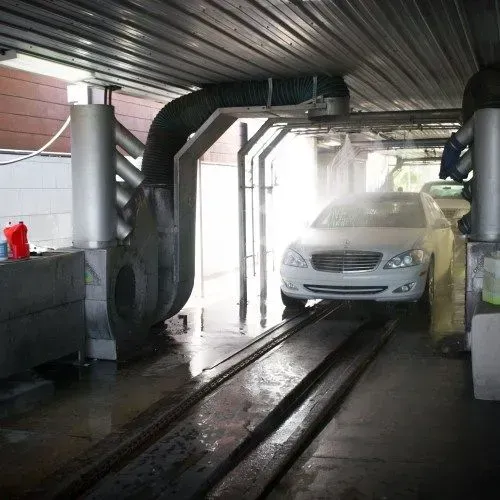 A car in an automated car wash. Water sprays, and the car is on a track.