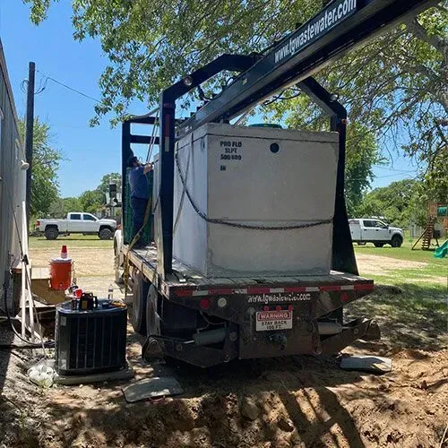 A flatbed truck with a large tank, in a yard, under a sunny sky.