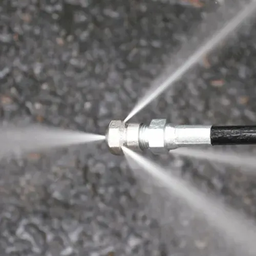 Water spraying from a pressure washer nozzle onto a dark gray surface.