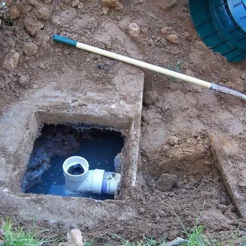 Open septic tank access point with exposed pipe and dark water.
