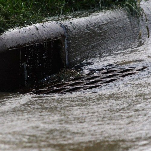 Flooding street drain, water flowing over curb and grate.