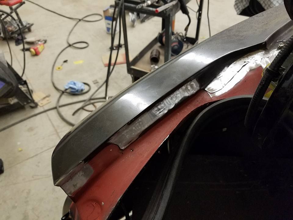 Close-up of a car body panel being repaired in a workshop, with tools and cables on the floor.