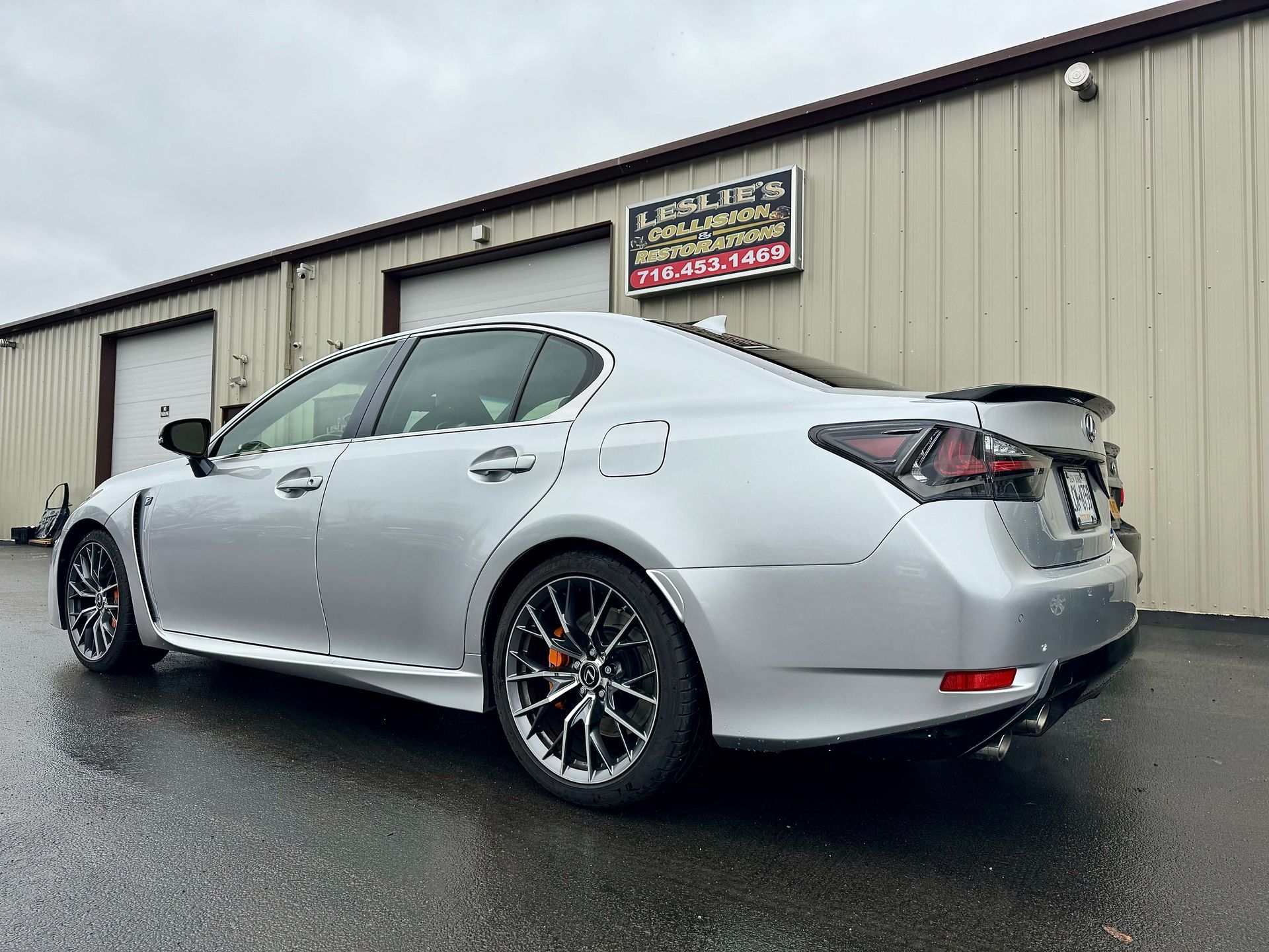 Silver sedan parked outside a beige industrial building on a wet day