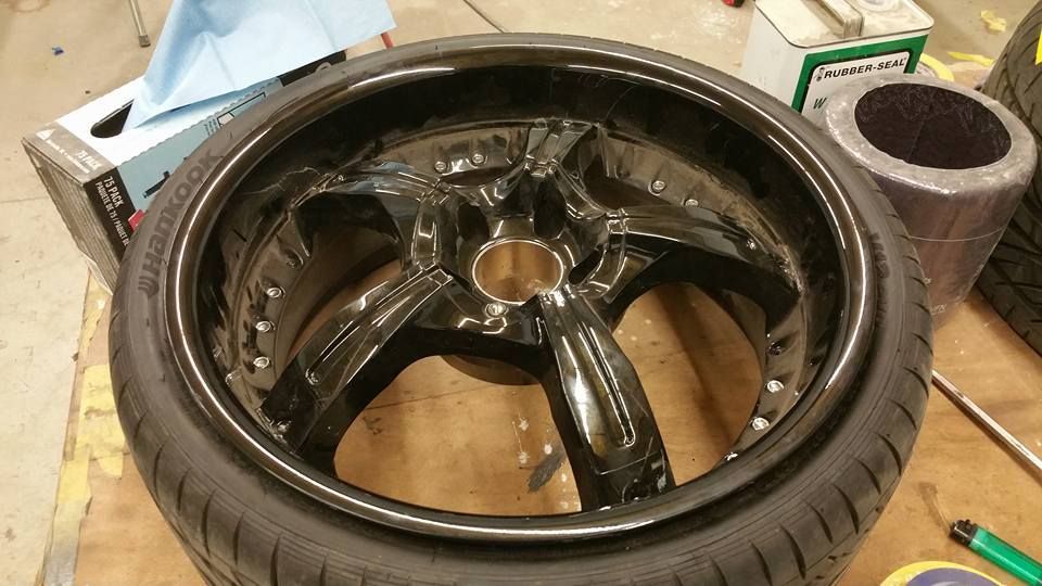 Black motorcycle wheel rim with tire, lying on a workshop floor with tools nearby