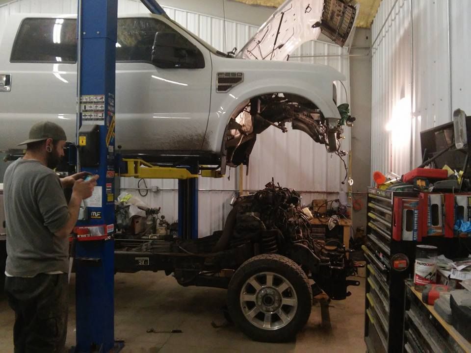 Silver truck cab lifted in an auto shop while a mechanic works on the exposed engine and chassis