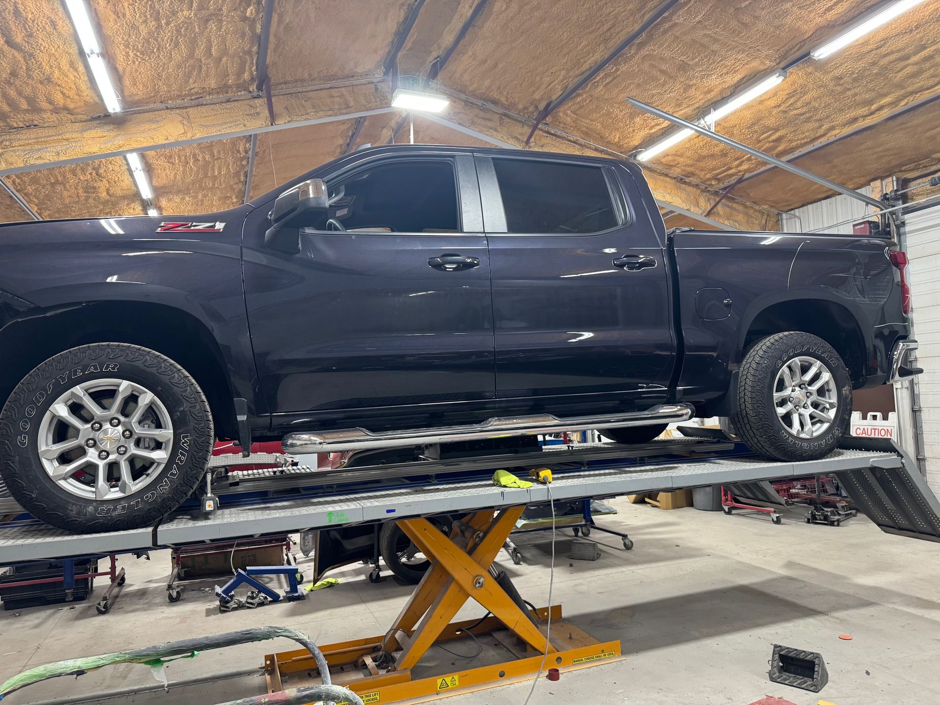 Black pickup truck on a hydraulic lift inside a garage with a vaulted wood ceiling