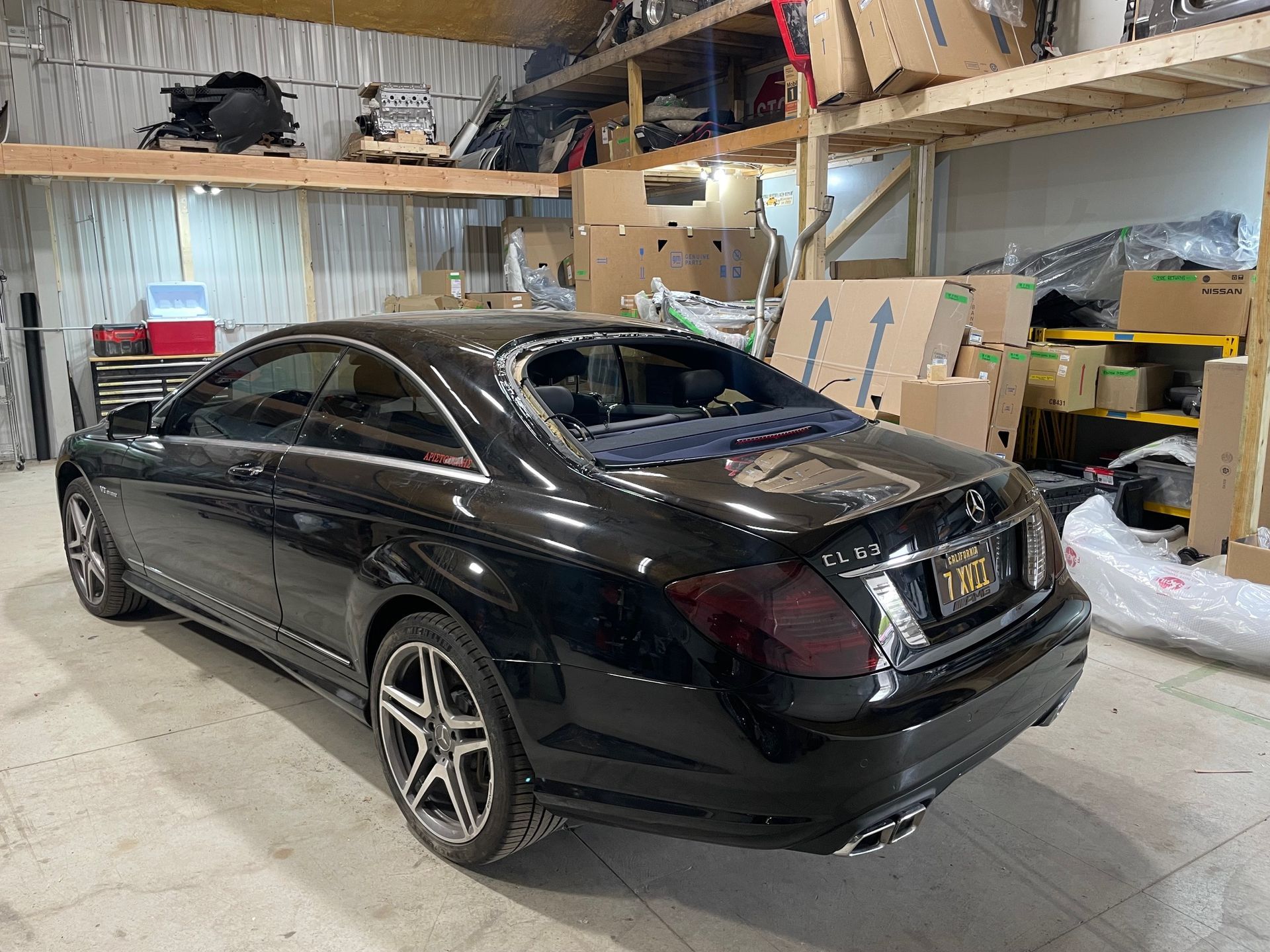 Black sedan parked inside a cluttered garage with shelves and boxes