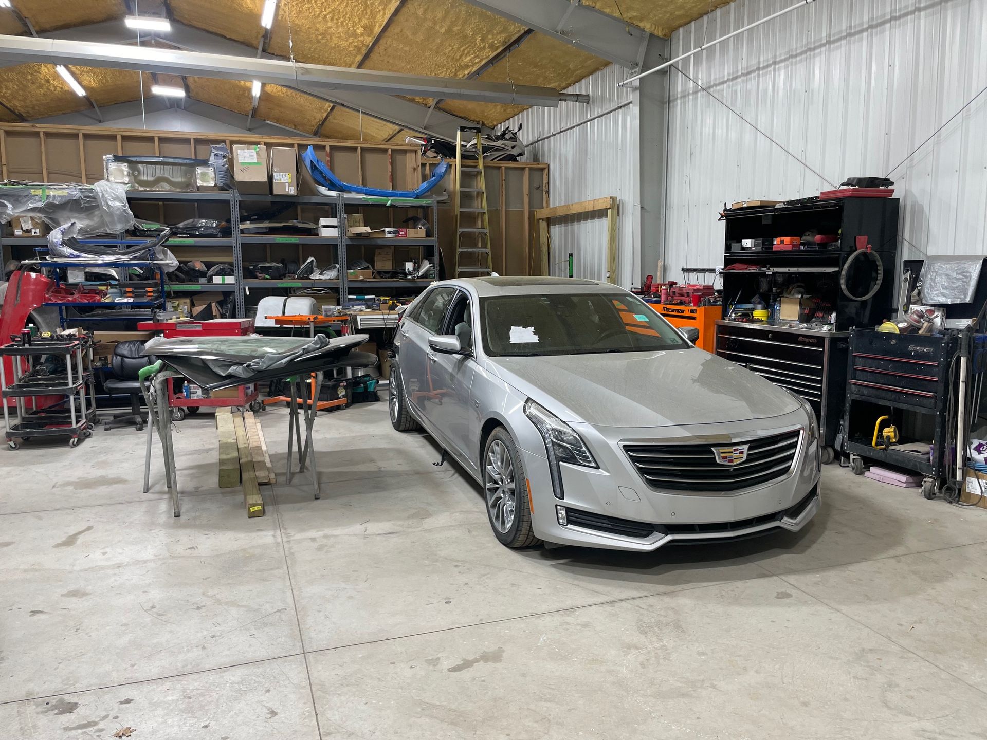 Silver sedan in an auto shop garage, surrounded by tools, shelves, and car parts.