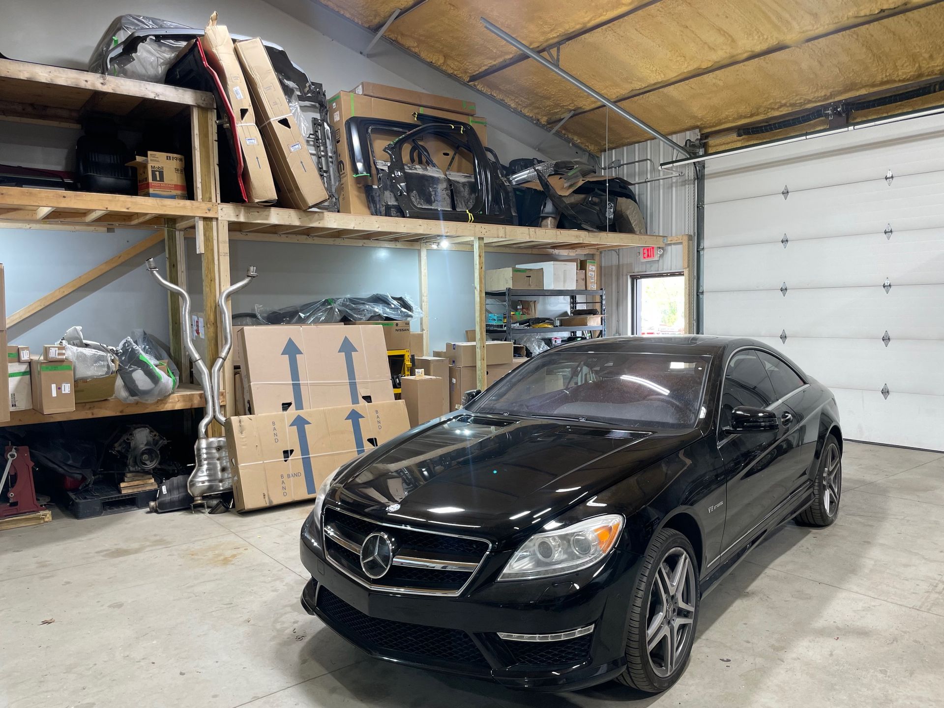 Black sedan parked inside a warehouse with shelves and stacked boxes nearby