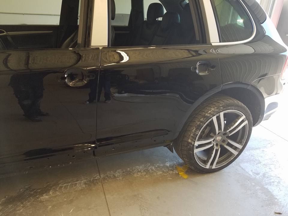 Black SUV parked in a garage, with a noticeable stain or spill on the floor near the rear wheel.