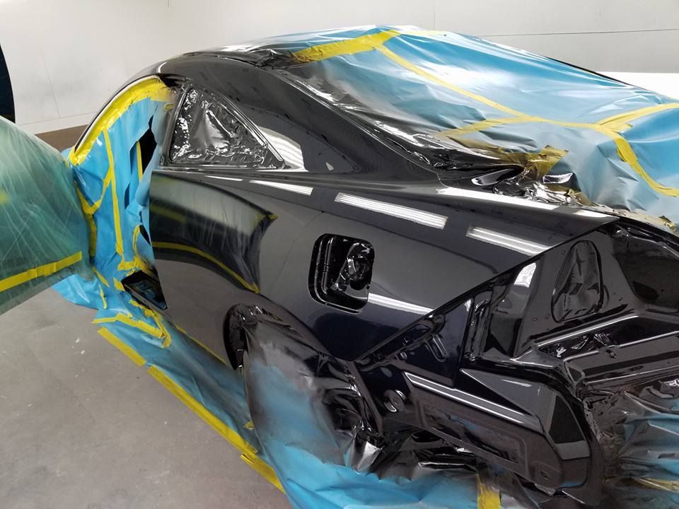 Damaged black car wrapped in blue and yellow protective film inside a garage