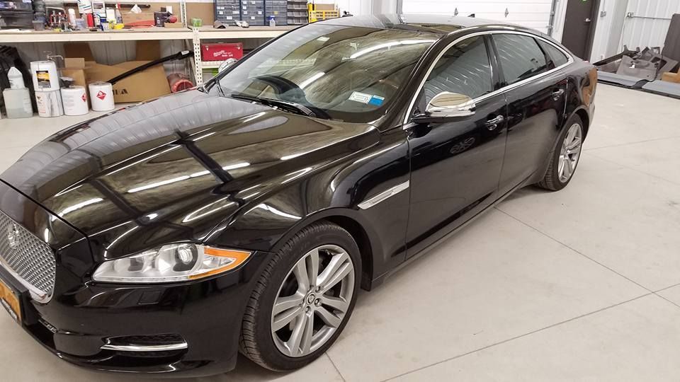 Black sedan parked inside a garage or workshop with shelves and equipment in the background