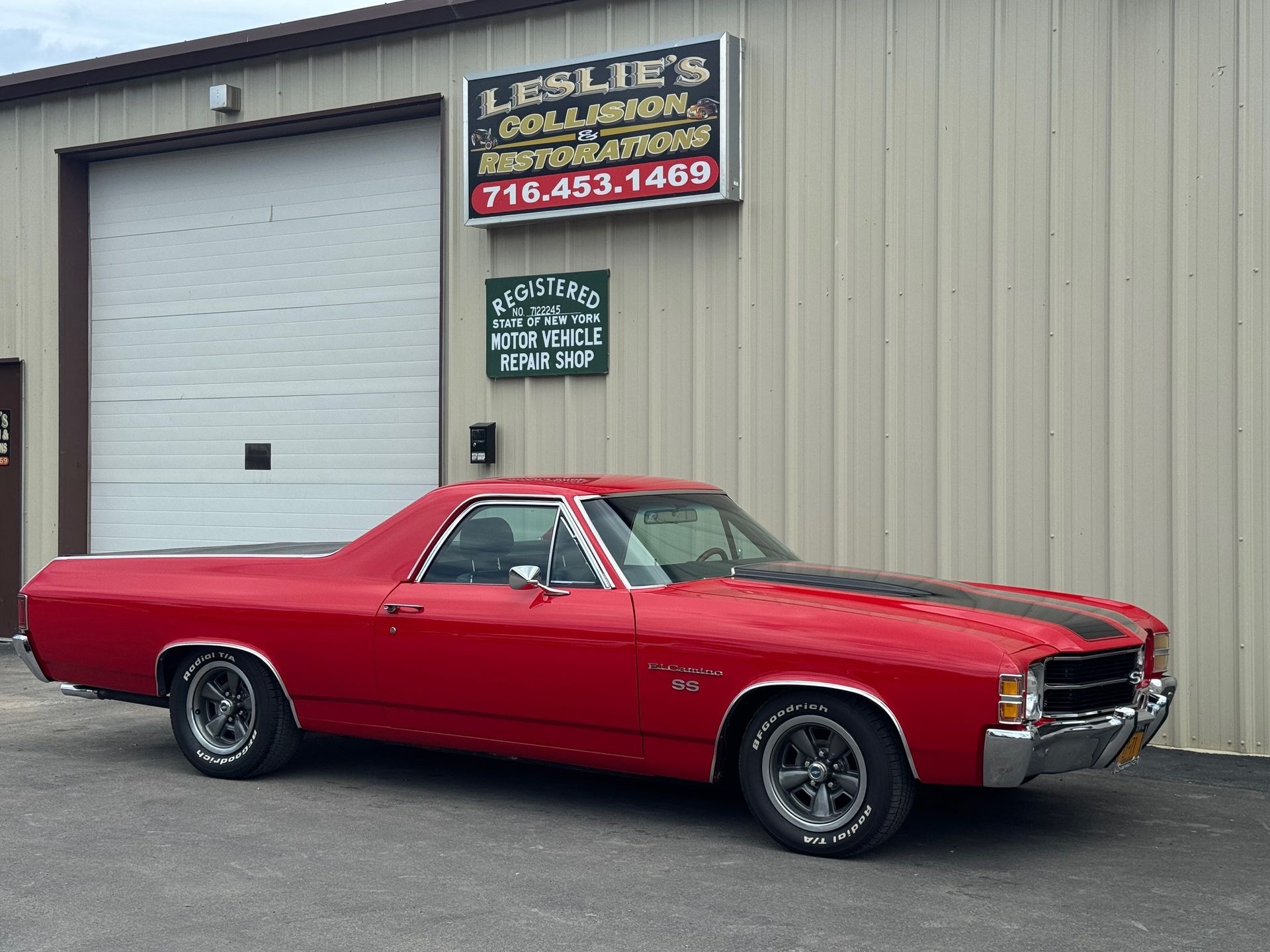 Red classic car parked outside a beige auto repair shop with a large garage door
