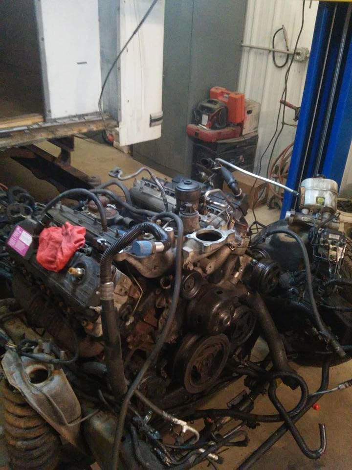 Several used car engines and hoses piled in a workshop garage with tools and equipment nearby