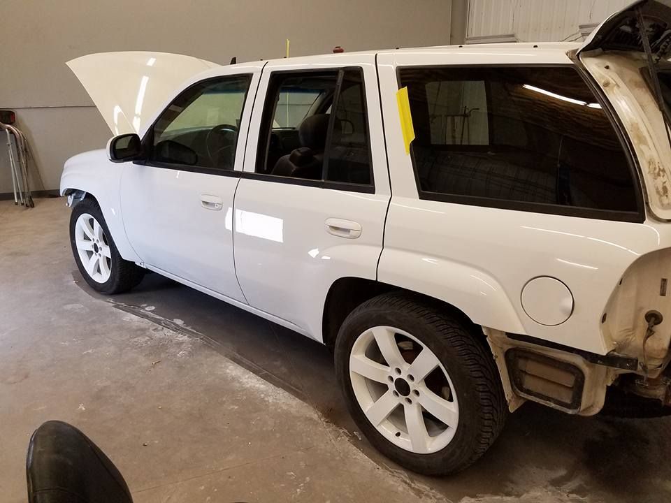 White SUV with front hood open, parked in a garage with visible rear body damage