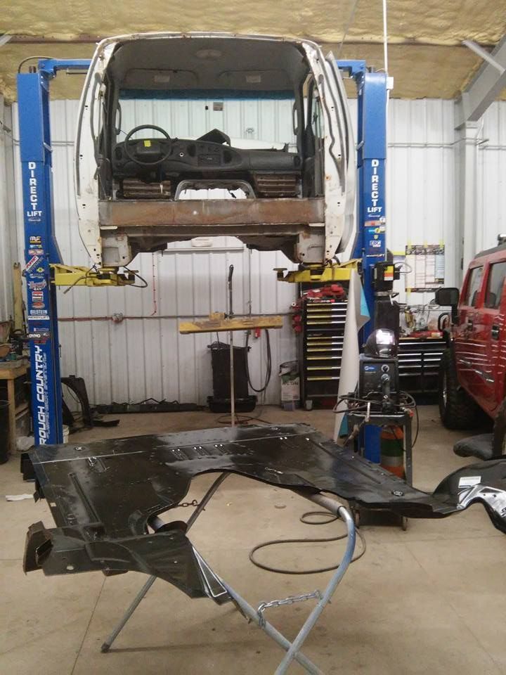 Car body lifted on a blue auto repair hoist in a workshop, with the chassis removed below.