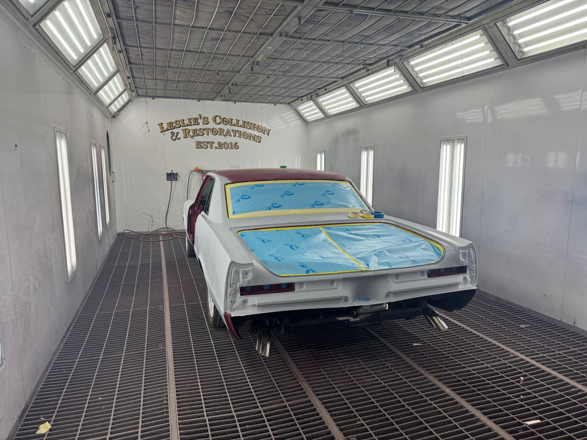 Car in a spray booth being painted white and blue, with masked windows and floor grating