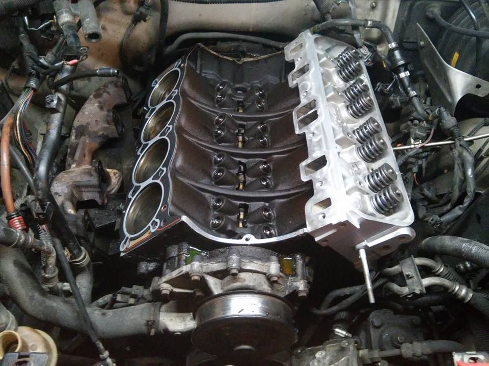 Car engine with intake manifold removed, exposing cylinders and engine components in a repair bay