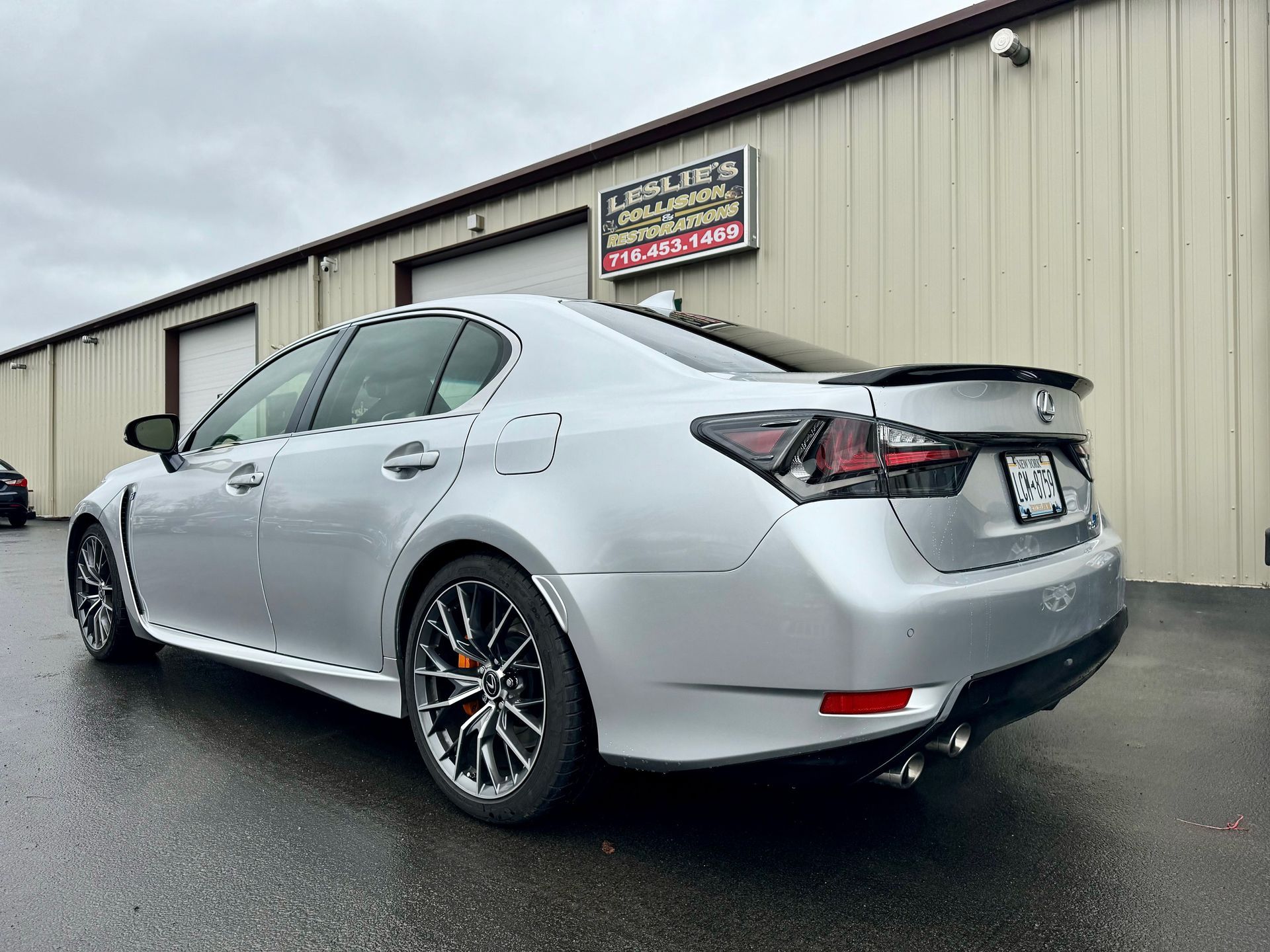 Silver sedan parked outside a beige industrial building on a wet lot