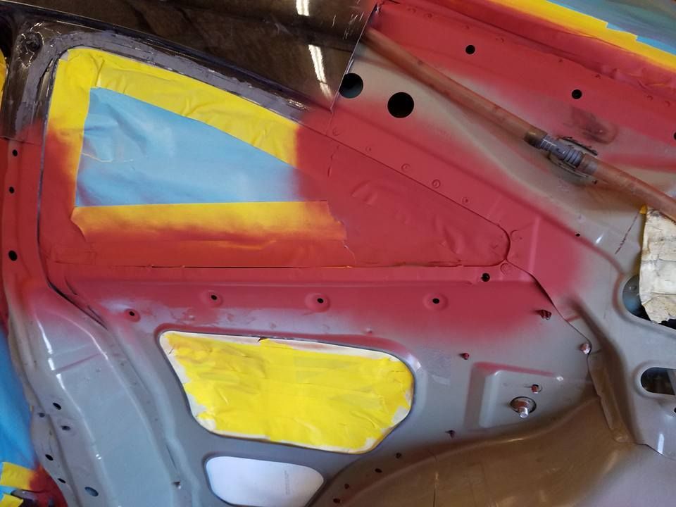Car door panel with red, yellow, blue, and gray painted sections and exposed interior metal.
