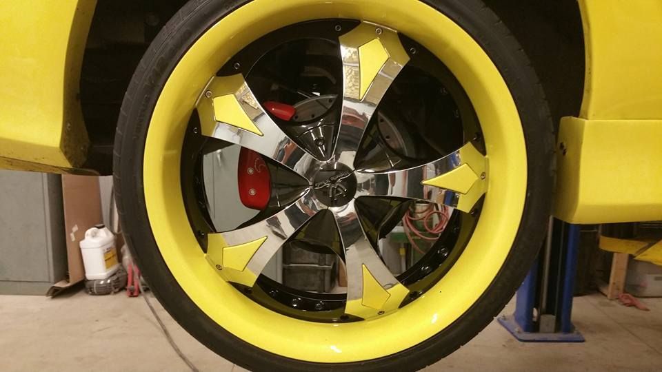 Close-up of a yellow toy car wheel with a chrome hubcap and white arrow decals