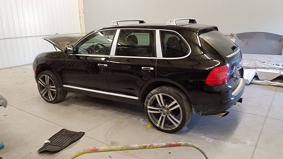 Black SUV in a garage, viewed from the side, with its rear hatch open and a hose on the floor.