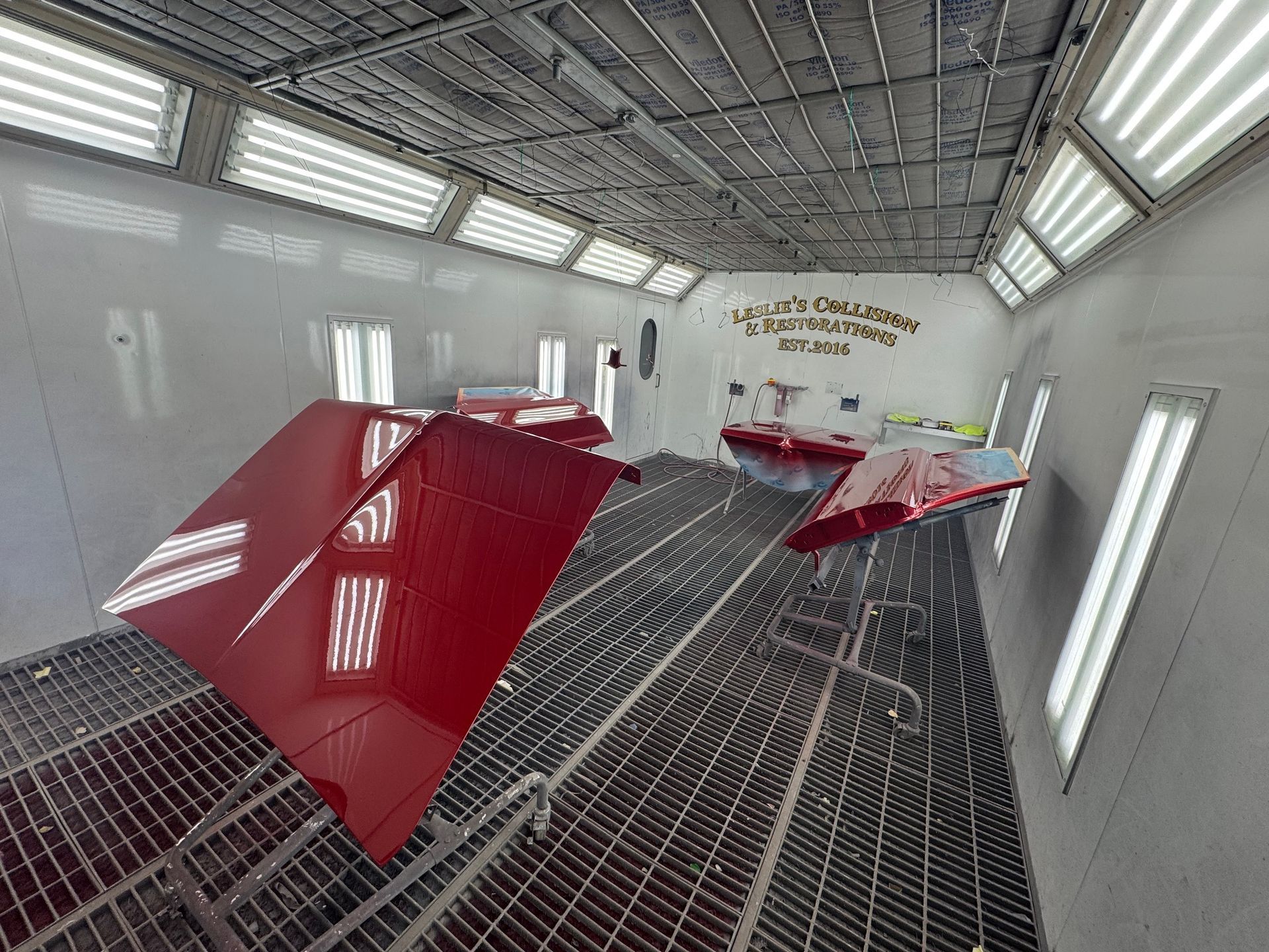 Automotive spray booth with red car parts drying on racks inside a clean white room