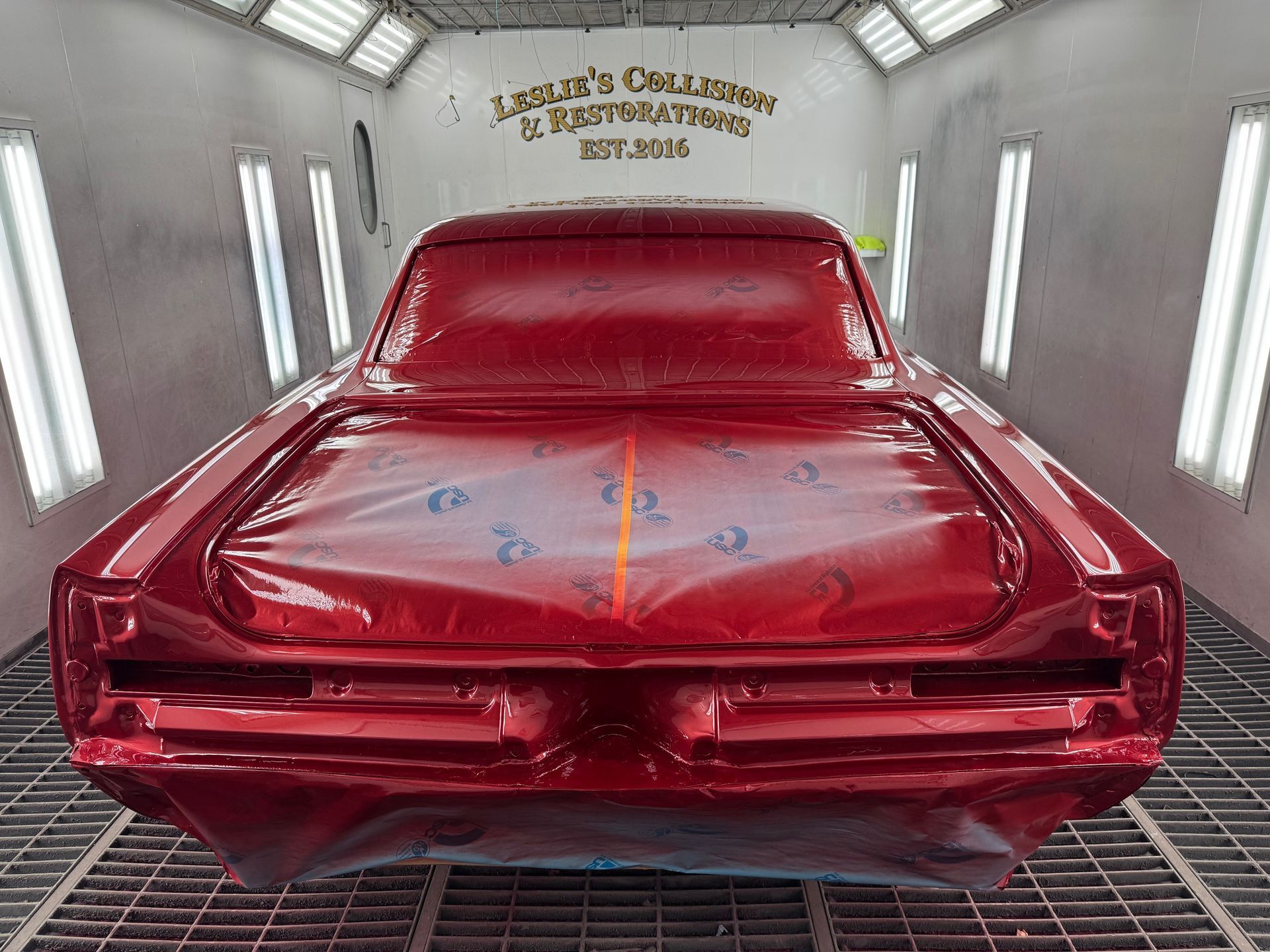 Red classic car in a spray booth, glossy finish with rear damage and red primer accents