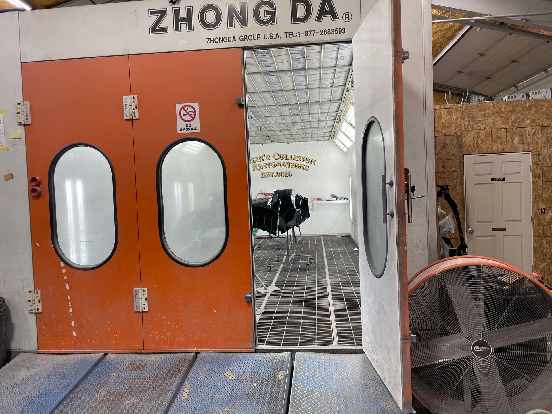 Orange double doors labeled “ZHONG DA” in an industrial workshop, with a large fan in front.