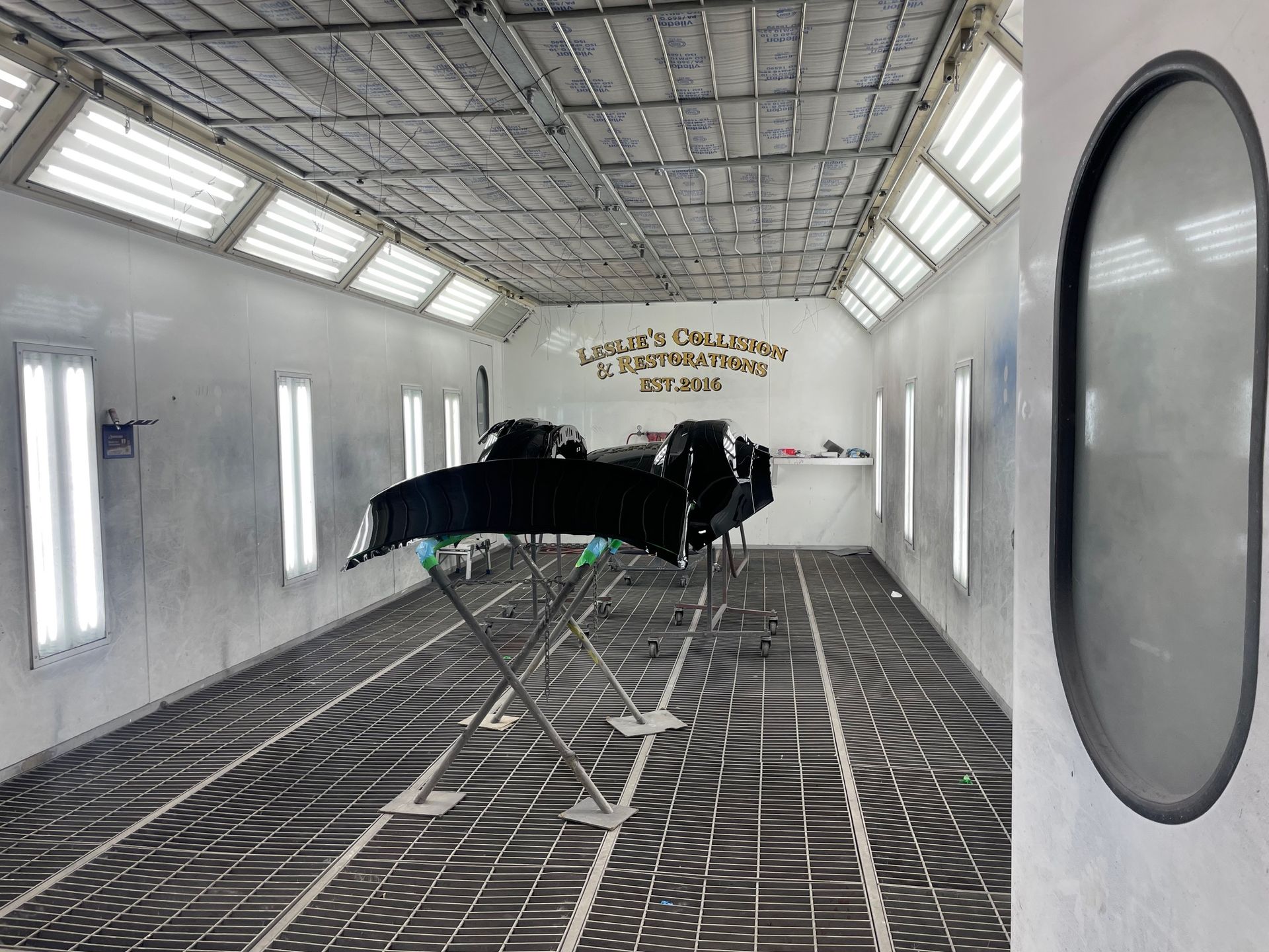 Black aircraft in a white spray booth with patterned floor and overhead lights