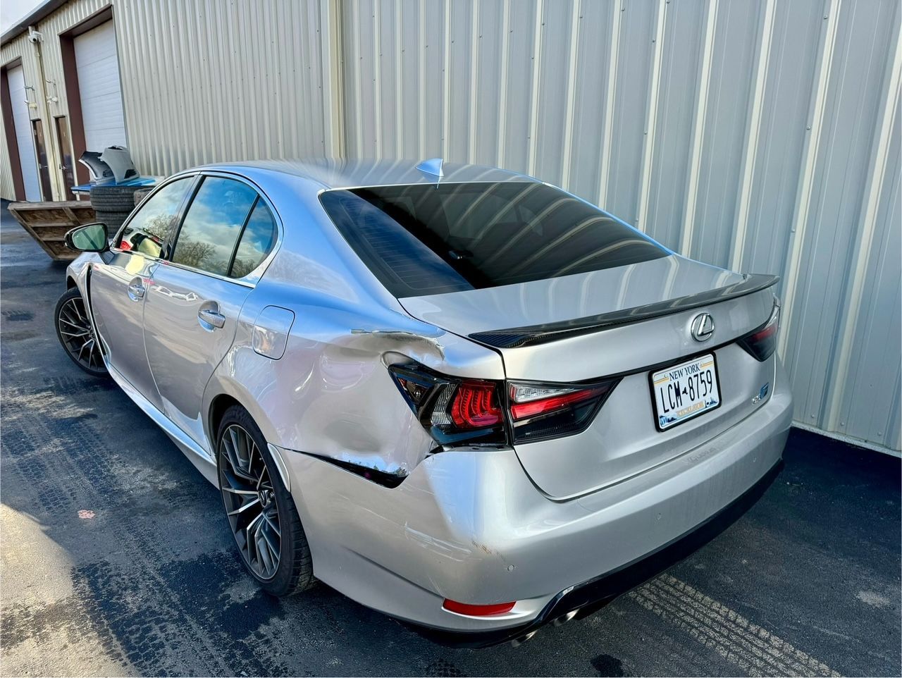 Silver sedan parked beside a corrugated metal building in an alley, rear three-quarter view.