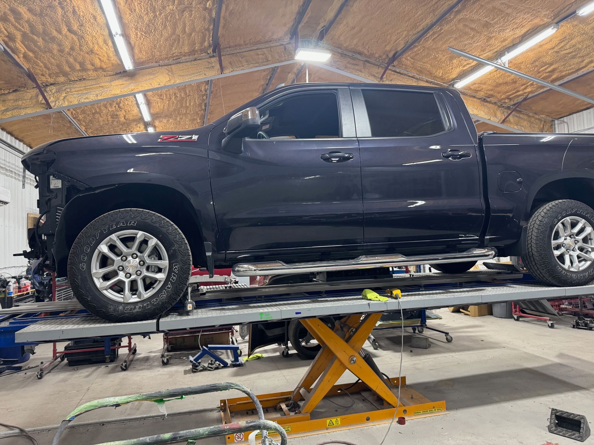 Black pickup truck on a lift in an auto shop, with the front end partially disassembled.