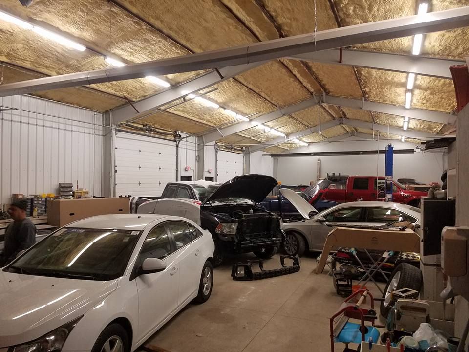 Large auto repair garage with several cars, one hood open, under exposed wooden roof beams.