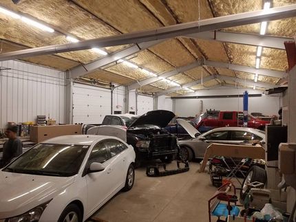 Auto repair shop interior with several cars, one raised on a lift and another with its hood open.