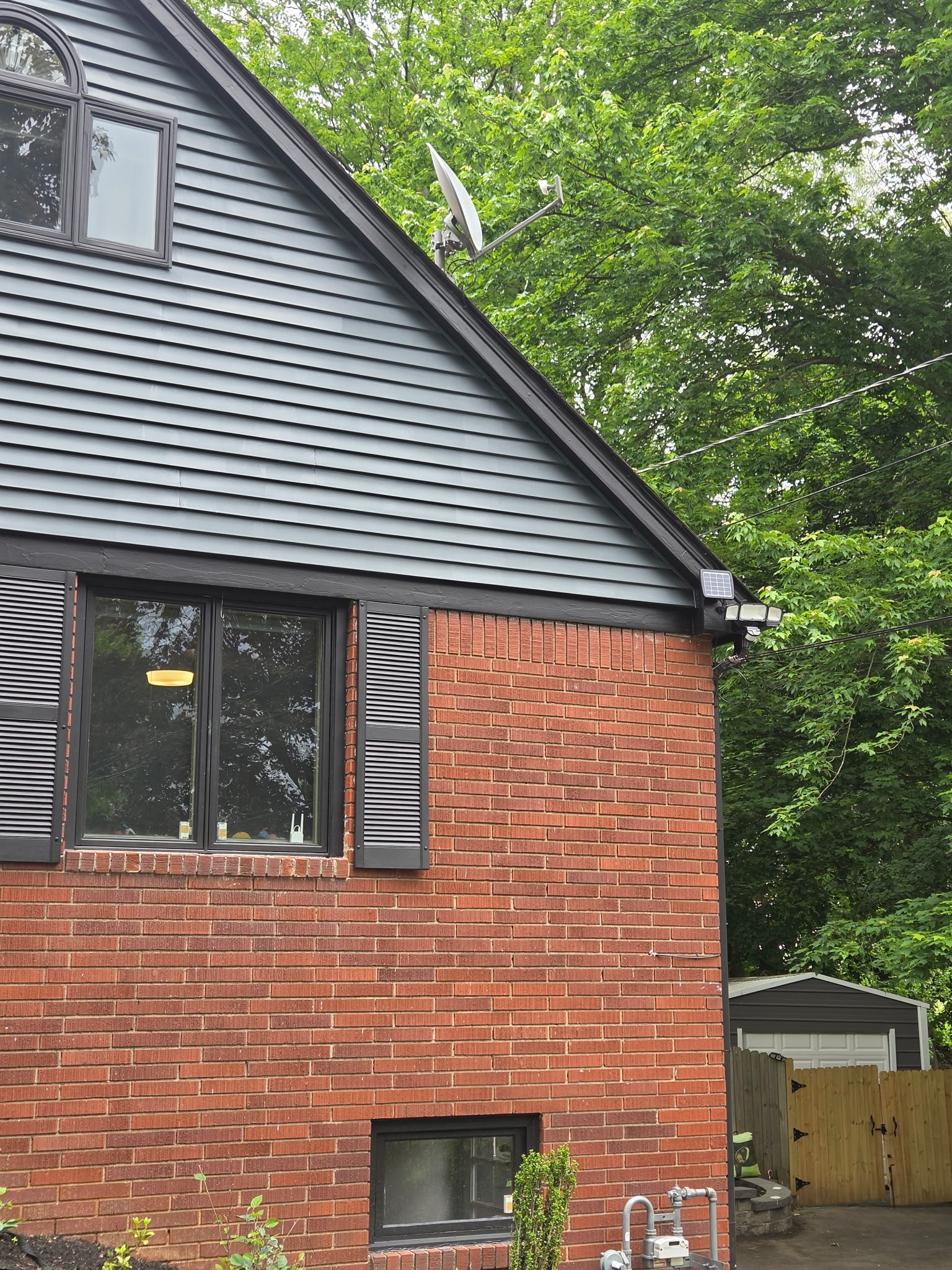 Brick-and-siding house exterior with a small window, gable roof, and trees in the background