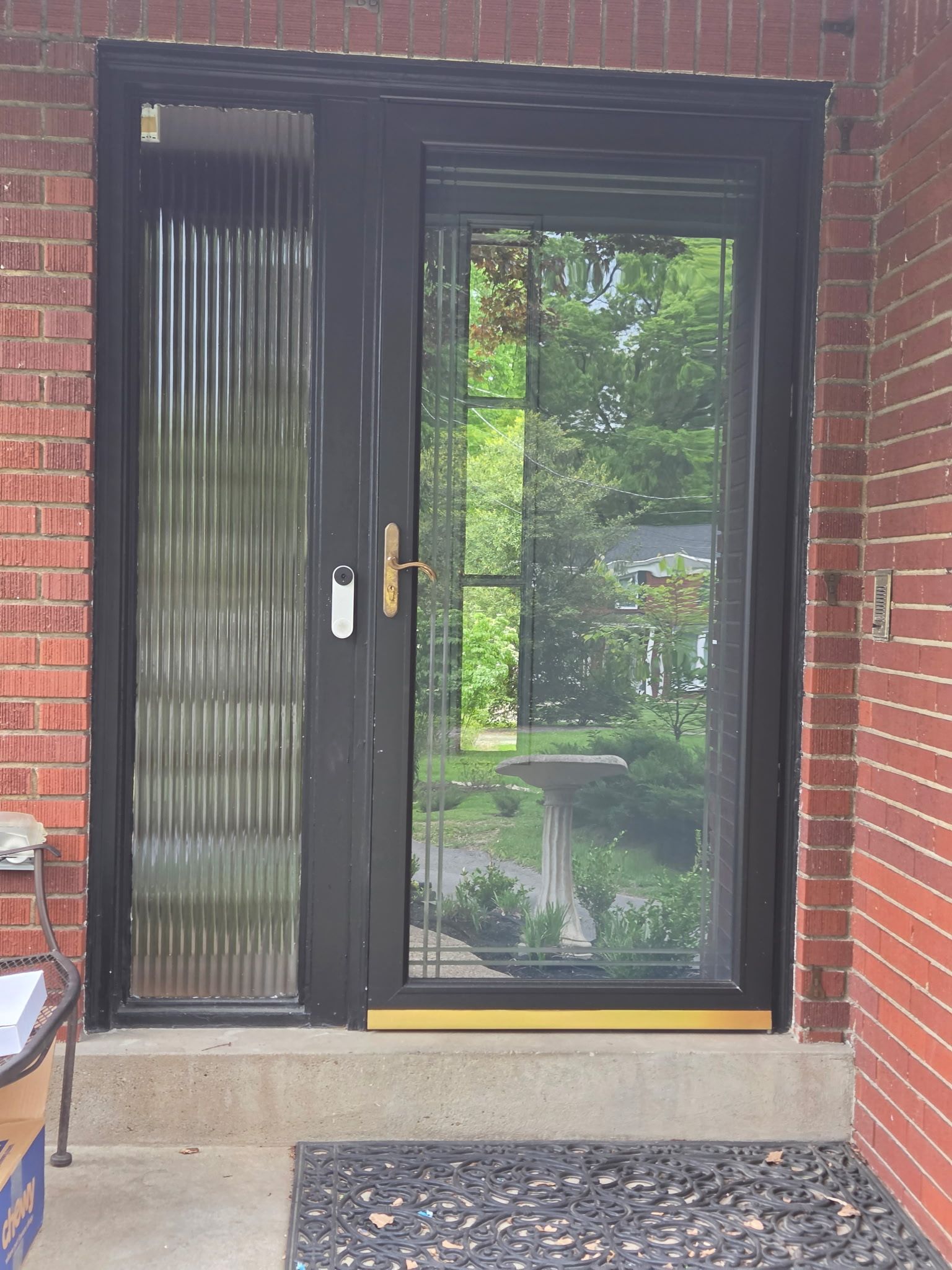 Black-framed glass door in a brick wall with blinds and a gold handle.