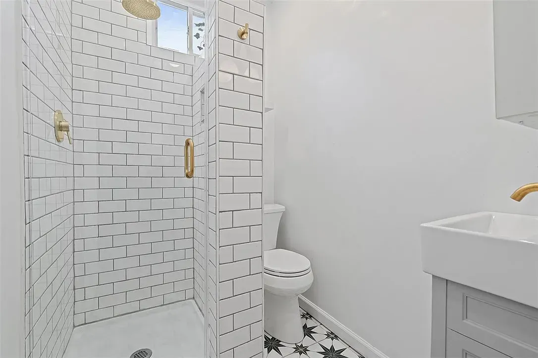 White bathroom with glass shower, toilet, and vanity sink on patterned floor tiles.