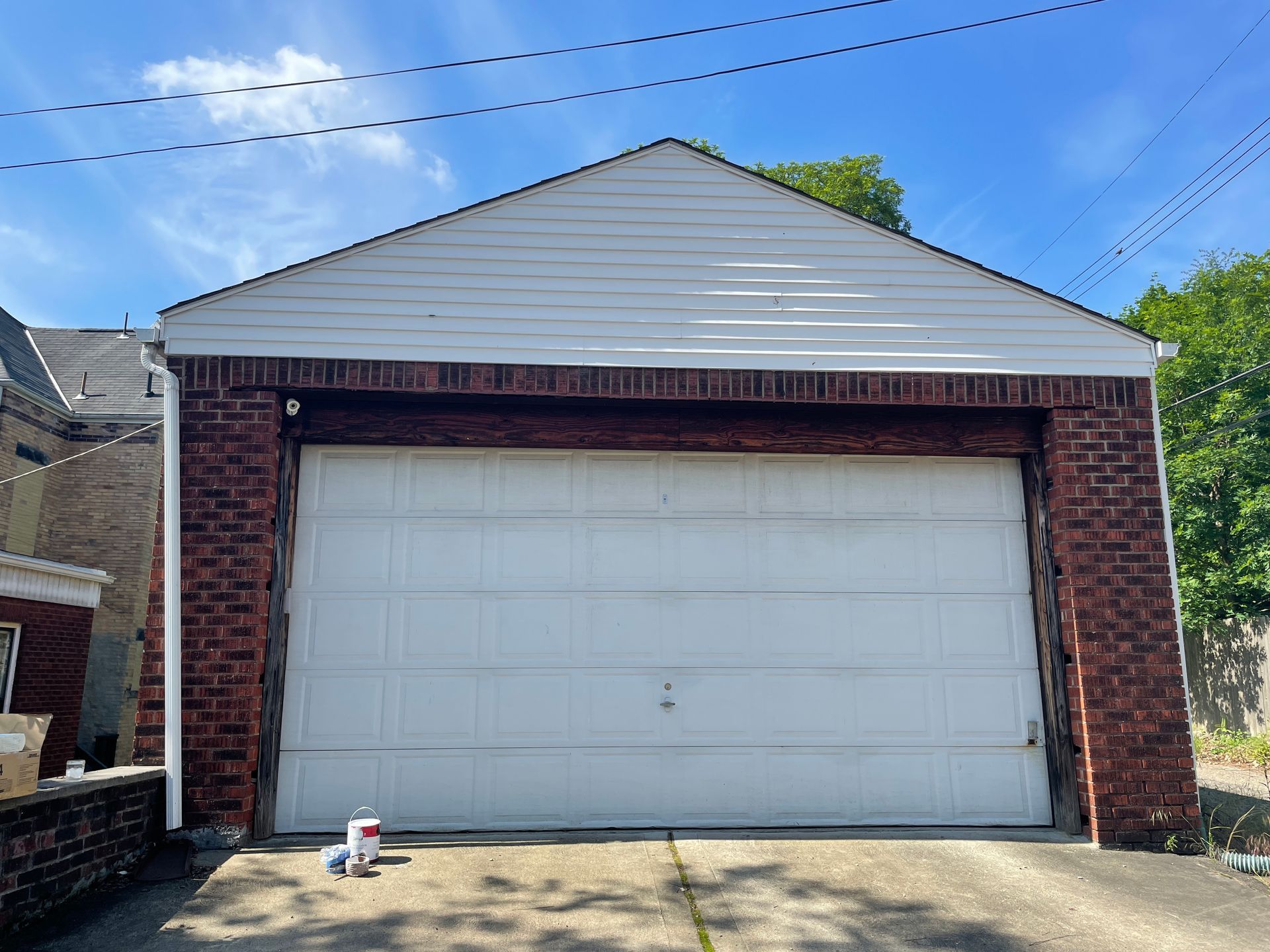 Detached brick garage with white double door, gray siding, and a small object on the driveway